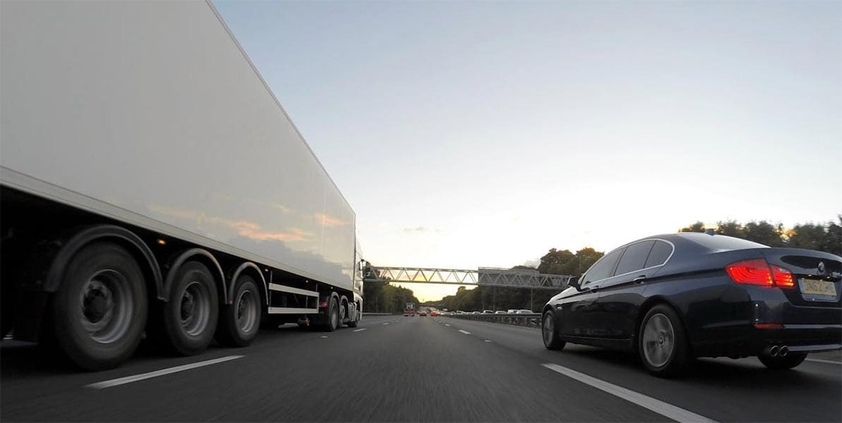 An 18-wheeler and a car driving down a highway